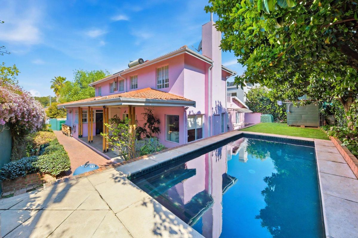 Rear exterior view of the house featuring a swimming pool, paved pool deck, and a covered patio area with a pink facade.