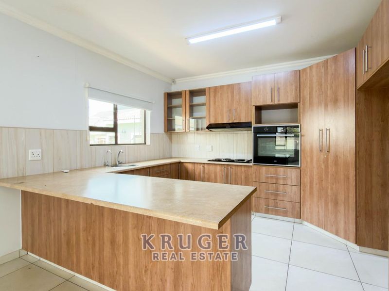 A clean, functional kitchen featuring wood-look cabinetry, laminate countertops, built-in oven, hob, and extractor fan with tiled flooring and backsplash.