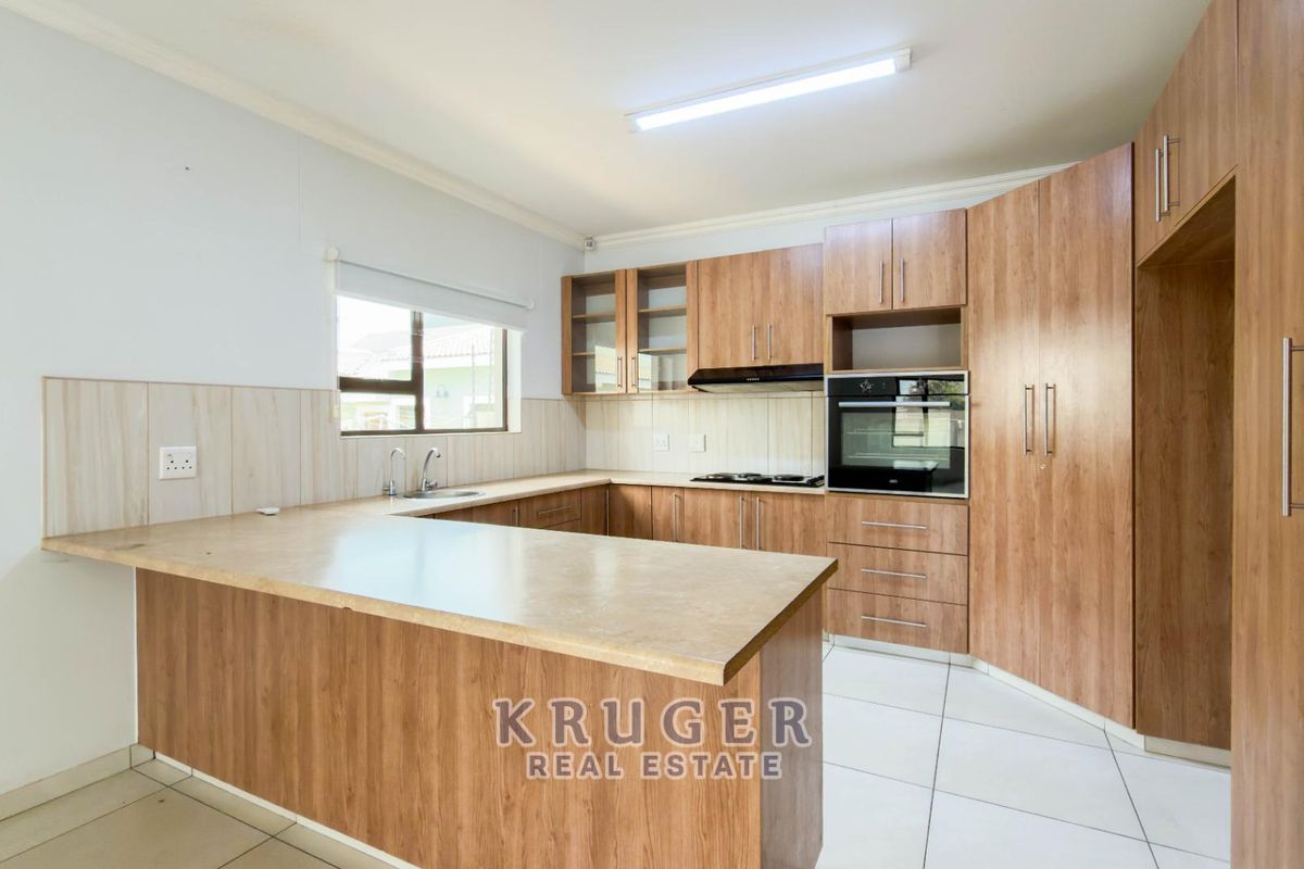 A clean, functional kitchen featuring wood-look cabinetry, laminate countertops, built-in oven, hob, and extractor fan with tiled flooring and backsplash.