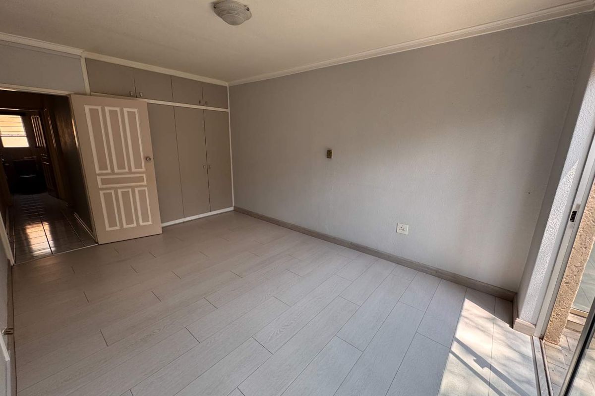 A bright, empty bedroom featuring neutral tiled flooring, built-in cupboards, and a sliding glass door providing access to the exterior.