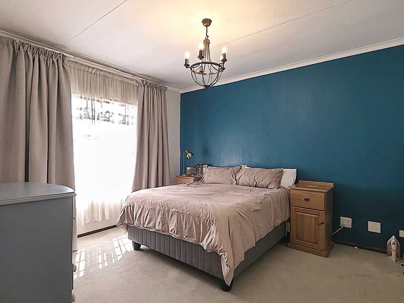 A well-lit bedroom featuring a prominent blue accent wall, neutral carpeting, and a central ceiling light fixture.