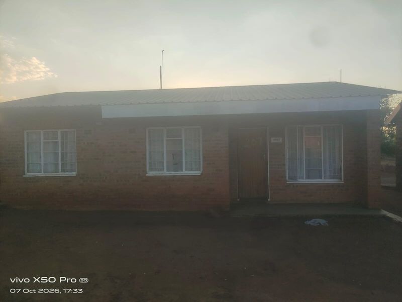 Front elevation of a single-story face brick house featuring a corrugated metal roof and standard window frames.