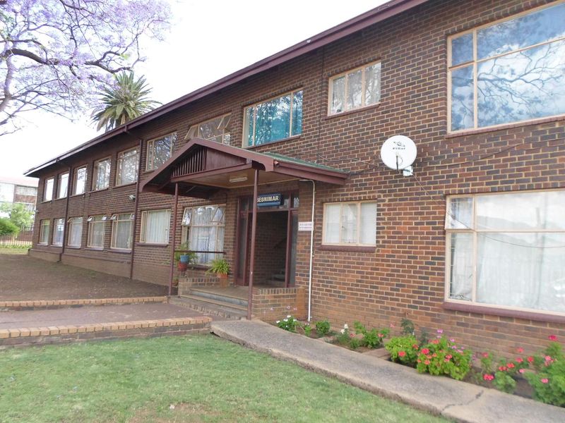 Exterior view of a multi-story apartment building featuring a face brick facade, covered entrance porch, and concrete walkway access.
