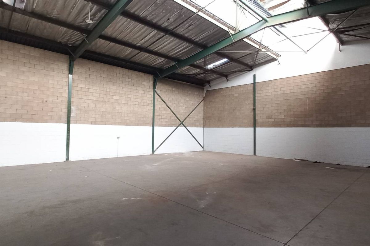 Spacious industrial warehouse unit featuring high ceilings, exposed steel structural beams, concrete flooring, and blockwork walls with natural light from roof panels.