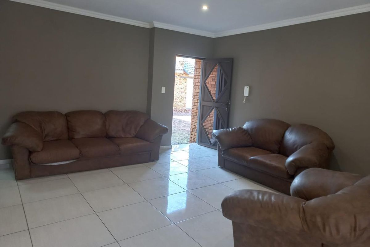 A spacious living room featuring neutral wall tones, large format floor tiles, and recessed lighting, providing a clean and functional base for living.