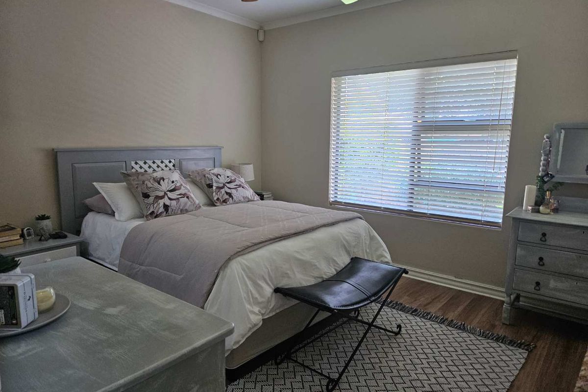 A well-maintained bedroom featuring wood-look flooring, a ceiling fan, and large windows with fitted blinds, offering a comfortable and neutral living space.