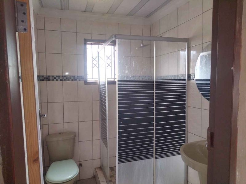 A functional bathroom featuring a shower enclosure, pedestal basin, and toilet with tiled wall finishes.