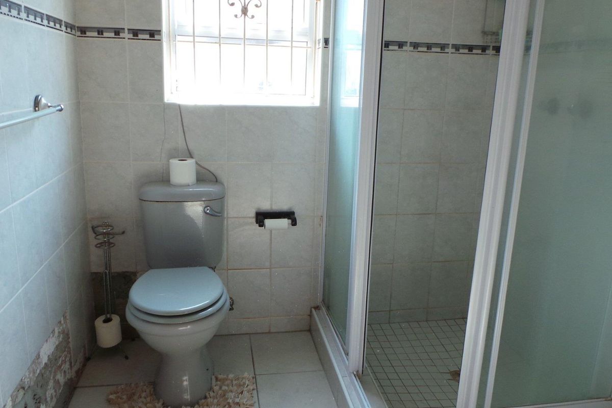 A functional bathroom featuring a shower enclosure, toilet, and tiled walls. The space shows signs of wear and requires cosmetic updates.