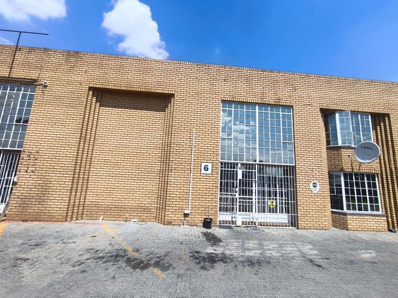 Front elevation of an industrial unit featuring face brick construction, a large roller shutter door, and secure steel-framed windows with security grilles.