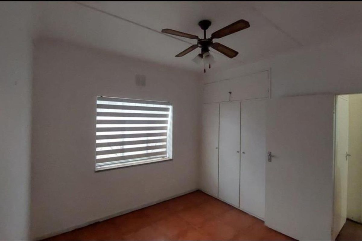 A bedroom featuring built-in cupboards, a ceiling fan, and tiled flooring, with a view into an adjacent hallway.