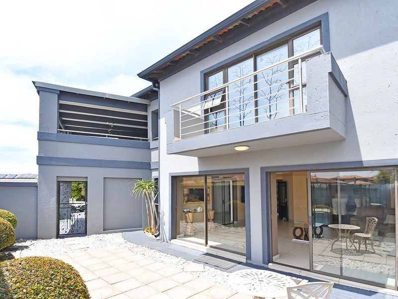 Rear view of the property featuring a paved patio area, sliding glass doors, and an upper-level balcony with metal railings.