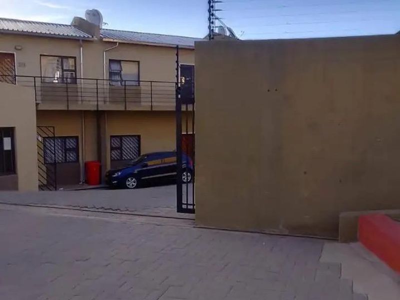 Exterior view of an apartment complex featuring a paved driveway, secure gated entrance, and perimeter electric fencing.