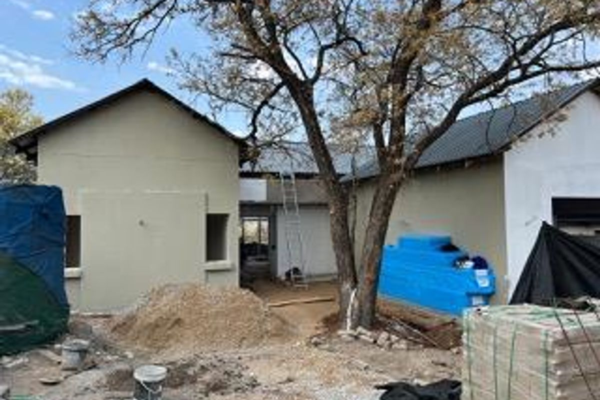 Rear view of a residential property currently undergoing construction, featuring plastered walls, a metal roof, and an installed water storage tank.