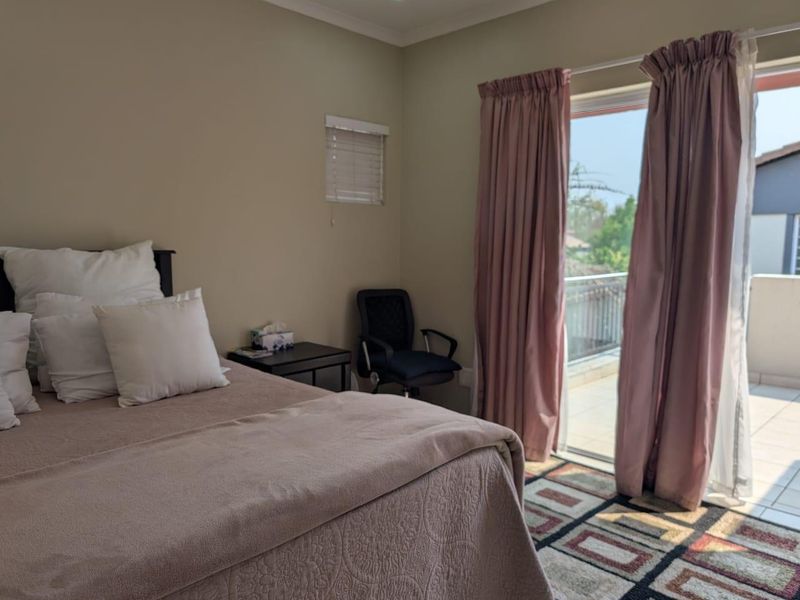 A bedroom featuring neutral walls, a sliding glass door providing access to a balcony, and a small window with a venetian blind.