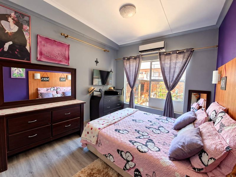 A well-maintained bedroom featuring laminate flooring, a split-system air conditioner, and a window with security bars, offering a comfortable and functional living space.