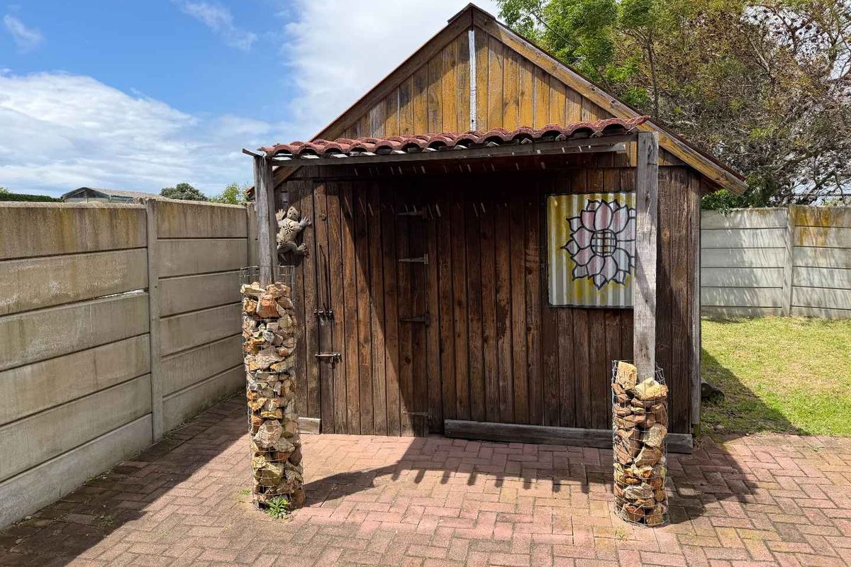 A rustic timber garden shed situated on a paved patio area, enclosed by precast concrete boundary walls and decorative gabion stone pillars.