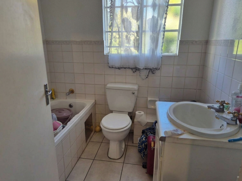A functional bathroom featuring a built-in bathtub, toilet, and vanity basin, with tiled walls and flooring throughout.