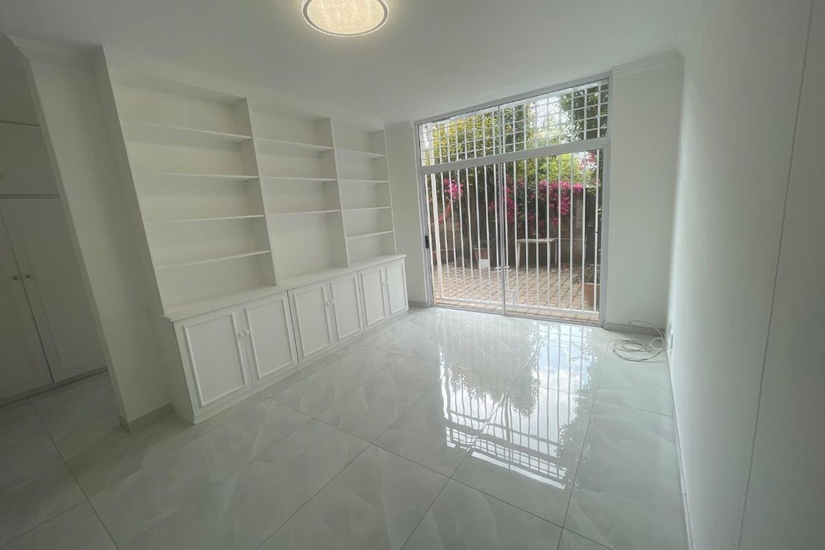 A bright, empty living room featuring polished tiled floors, extensive built-in cabinetry with shelving, and a sliding glass door leading to a private patio.
