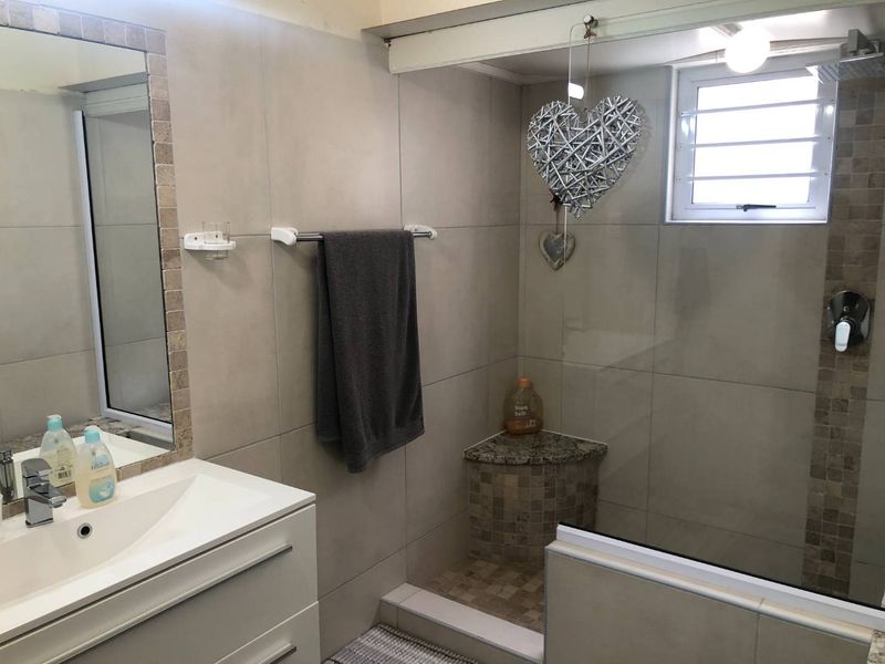 Modern bathroom featuring a walk-in shower with a built-in granite corner seat, glass enclosure, and a contemporary vanity with a basin.