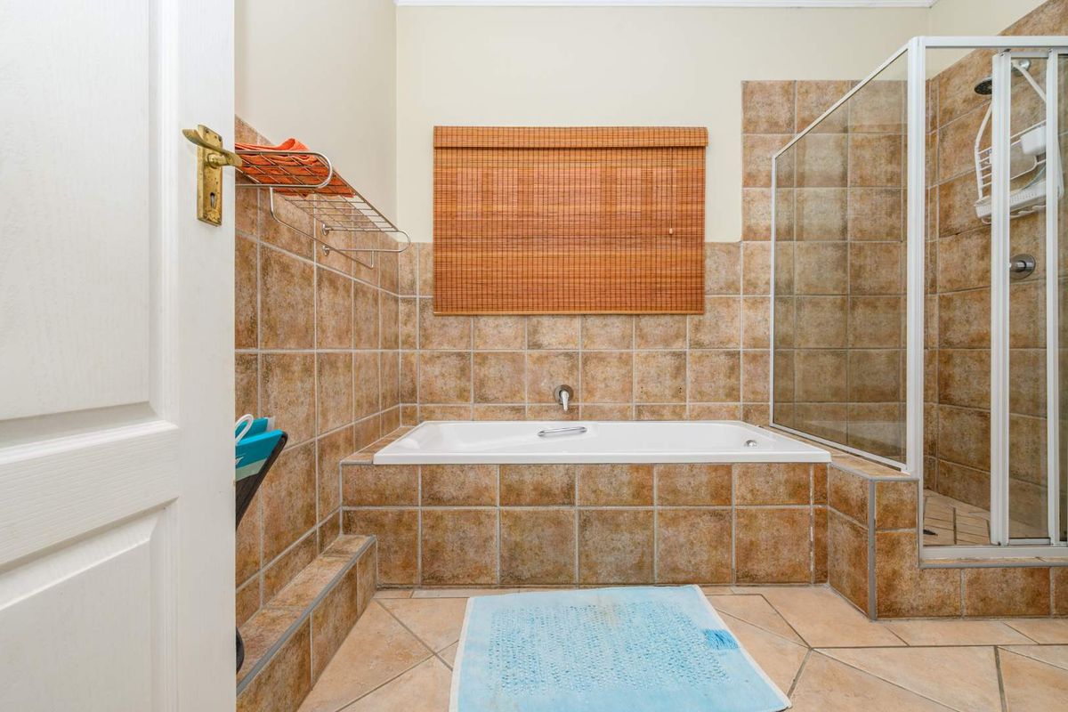 A functional bathroom featuring a built-in bathtub, separate shower enclosure, and neutral ceramic tiling throughout.