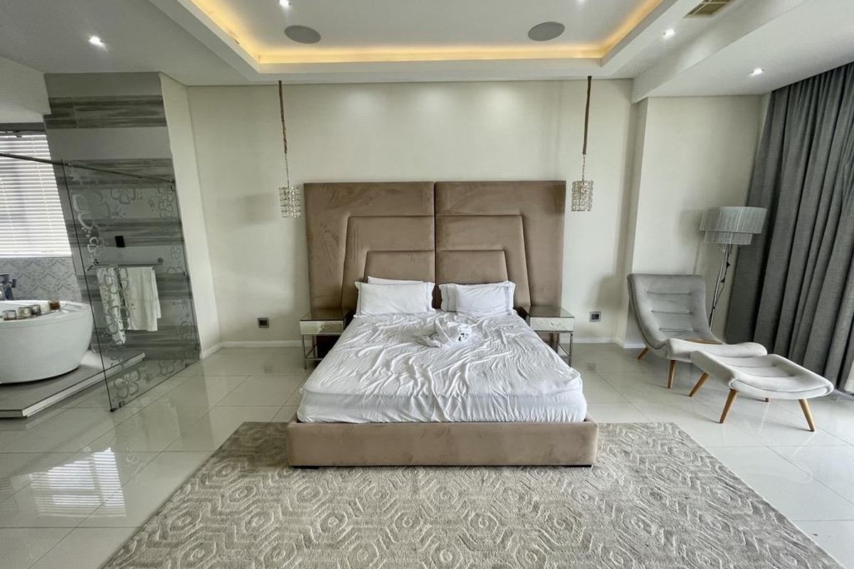 Spacious master bedroom featuring a modern recessed ceiling, integrated lighting, and an open-plan glass-enclosed en-suite bathroom with a soaking tub.