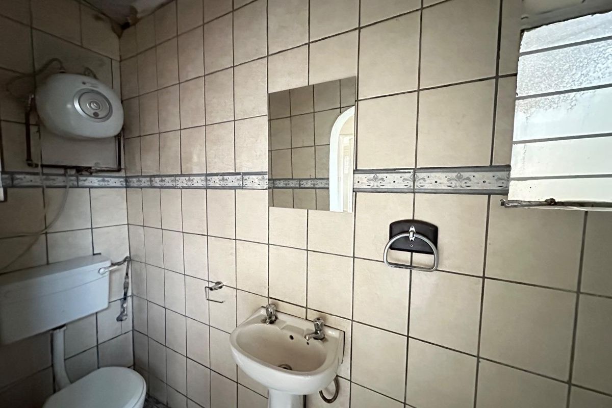 A dated bathroom featuring ceramic wall tiles, a pedestal basin, a toilet, and an electric water heater unit.
