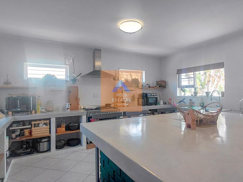 Spacious kitchen featuring a large concrete island, built-in concrete countertops, stainless steel extractor fan, and tiled flooring with ample open shelving.