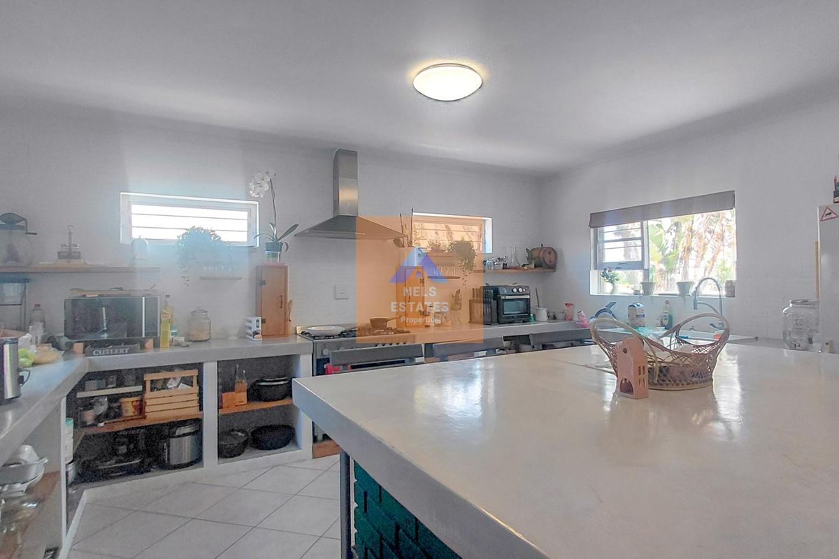 Spacious kitchen featuring a large concrete island, built-in concrete countertops, stainless steel extractor fan, and tiled flooring with ample open shelving.