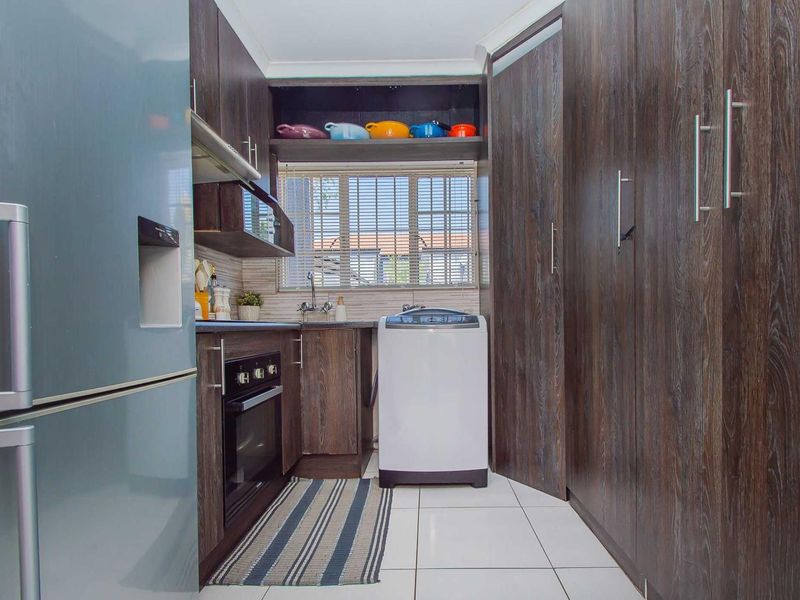 Compact kitchen featuring dark wood-finish cabinetry, built-in oven, extractor fan, and tiled flooring with a functional layout.