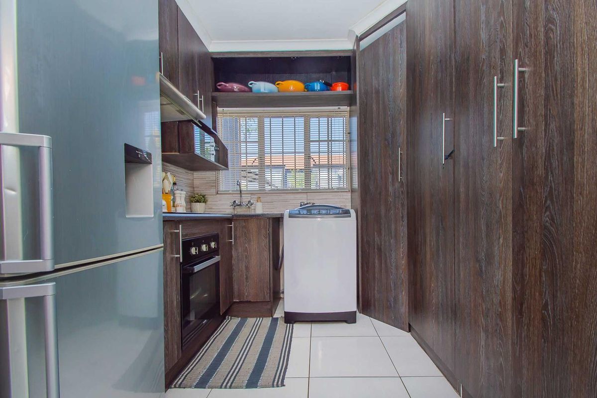 Compact kitchen featuring dark wood-finish cabinetry, built-in oven, extractor fan, and tiled flooring with a functional layout.