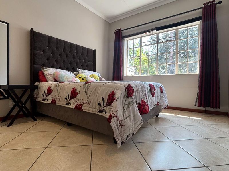 A well-lit bedroom featuring neutral tiled flooring, large windows with curtain rails, and classic skirting boards, offering a comfortable and functional living space.