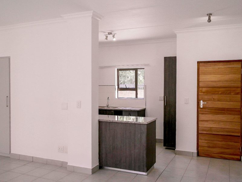 An open-plan kitchen area featuring granite countertops, dark cabinetry, tiled flooring, and a wooden door, presenting a clean and functional layout.
