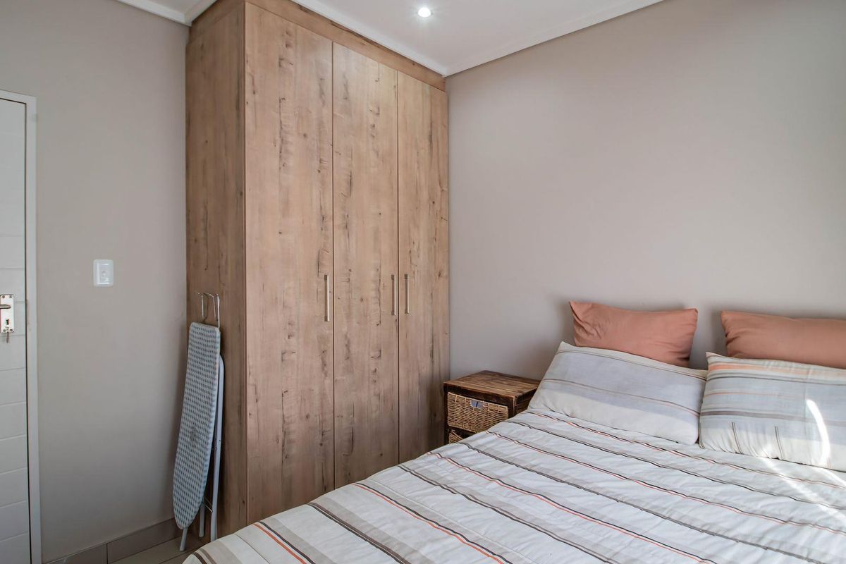 A well-maintained bedroom featuring neutral wall tones and a modern, wood-finish built-in wardrobe providing ample storage space.