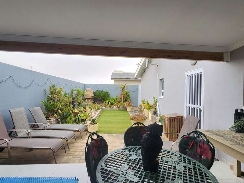 A covered patio area overlooking a landscaped rear garden with paved flooring and secure access to the main dwelling.