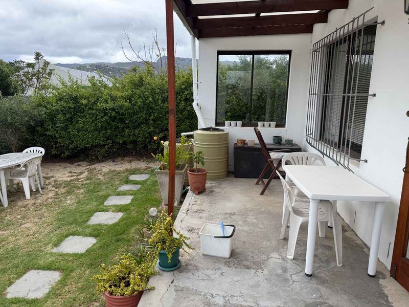 A covered patio area featuring a timber pergola, concrete flooring, and direct access to the garden through sliding glass doors with security bars.