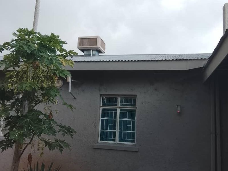 Rear exterior view of the property featuring a corrugated metal roof, an evaporative cooling unit, and a paved patio area.