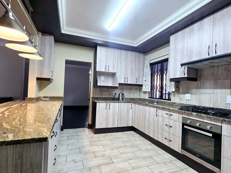 Modern kitchen featuring granite countertops, light wood-finish cabinetry, built-in oven with gas hob, and stylish pendant lighting.
