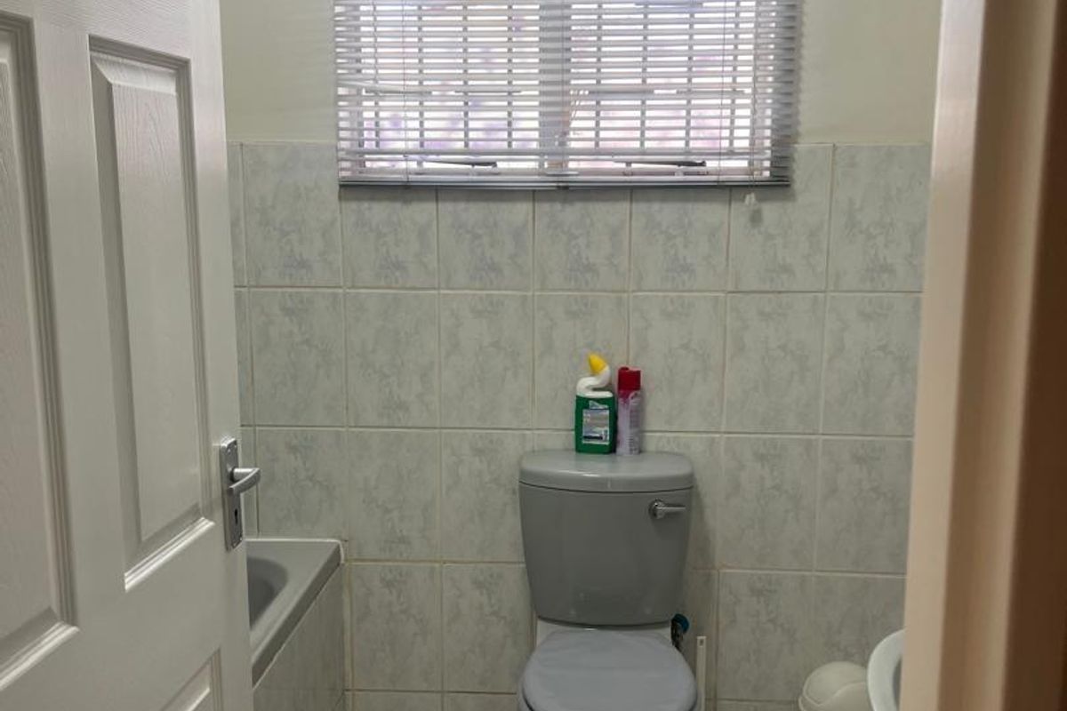 A functional bathroom featuring tiled walls and flooring, a standard toilet, and a bathtub with a window fitted with venetian blinds.