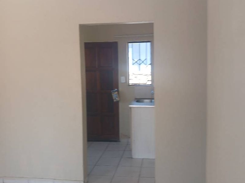 An empty open-plan living area featuring tiled flooring and neutral walls, with a view through to a secondary space or kitchen area.