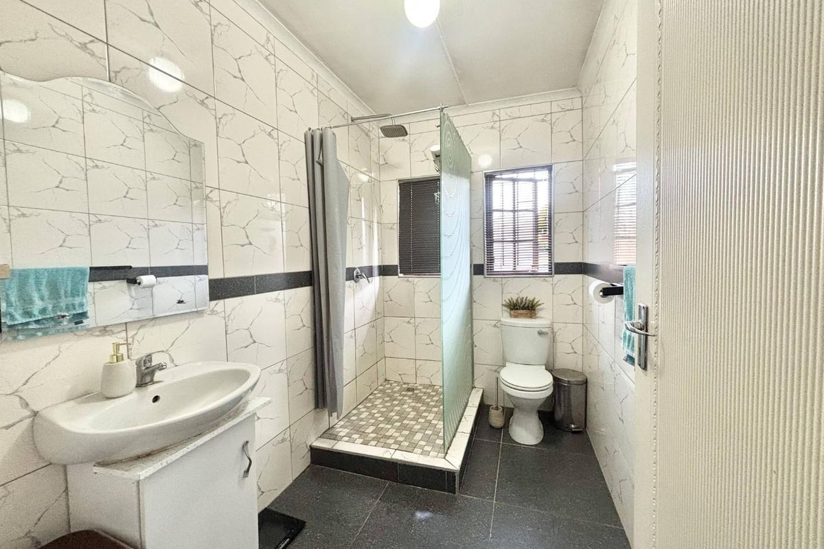 A functional bathroom featuring a walk-in shower with a glass screen, vanity basin, and toilet, finished with marble-effect wall tiles and dark floor tiles.