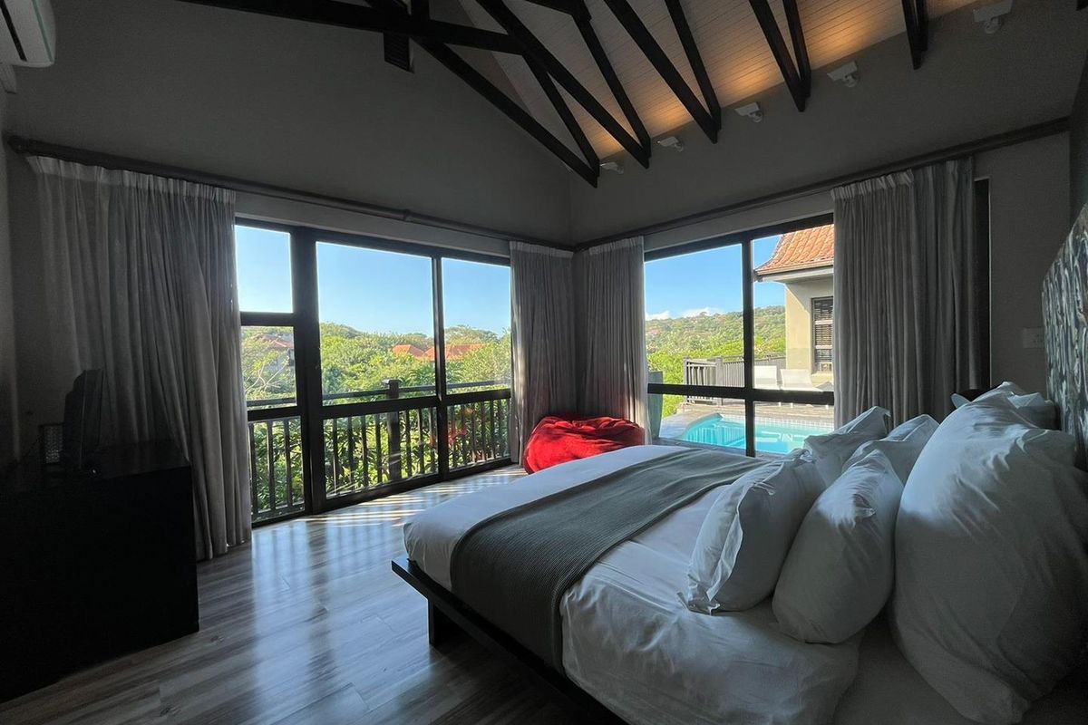 Spacious bedroom featuring high vaulted ceilings with exposed beams, large windows with scenic views, and direct access to an outdoor pool area.