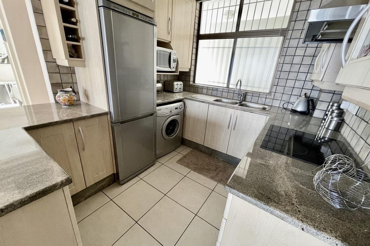 Compact kitchen featuring light wood-tone cabinetry, granite countertops, integrated stainless steel appliances, and tiled flooring with a functional layout.