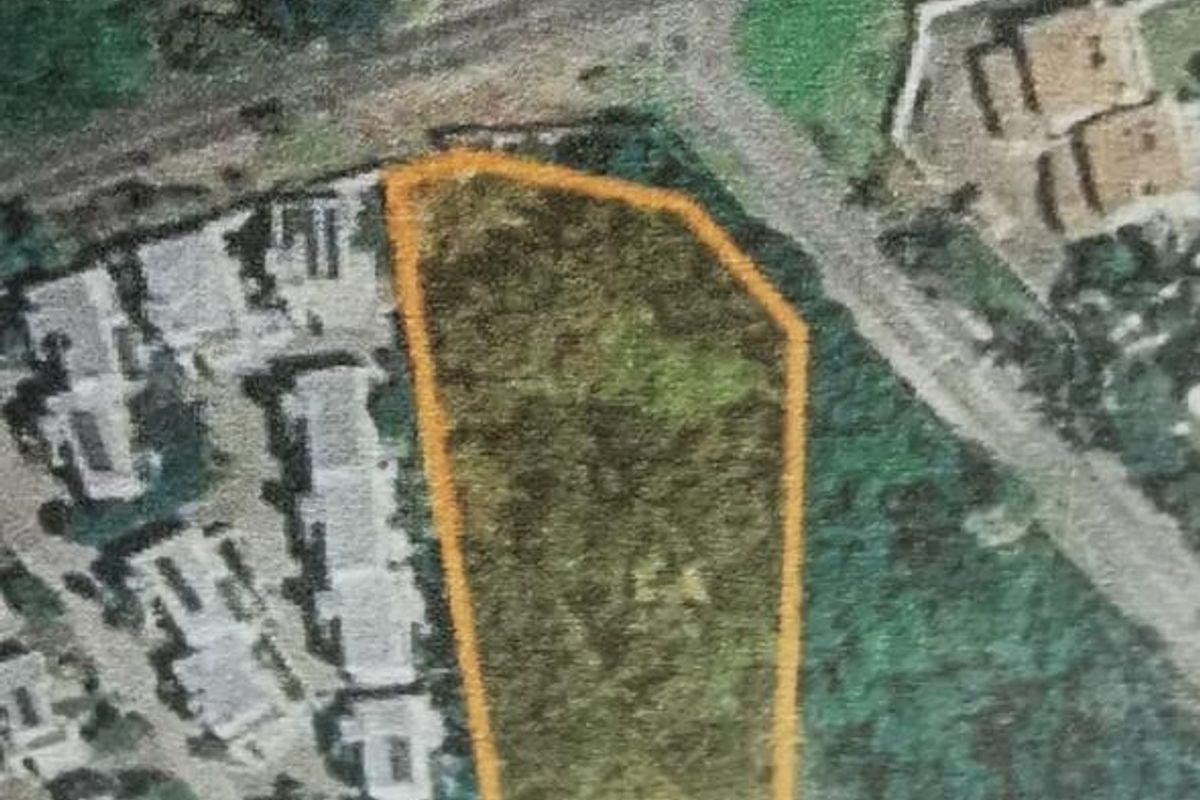 An aerial view of a vacant residential plot highlighted with an orange boundary, situated within an established neighborhood.