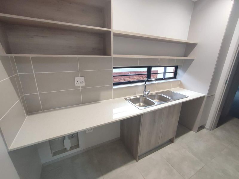 A modern, clean scullery featuring quartz countertops, double bowl sink, built-in cabinetry, and open shelving, providing ample prep and wash-up space.
