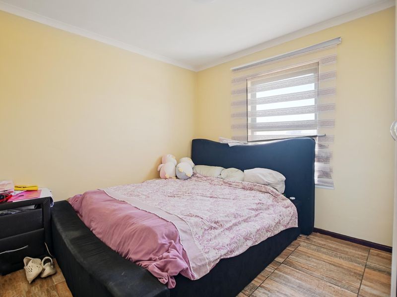 A functional bedroom featuring tiled flooring, neutral wall finishes, and a window fitted with modern roller blinds.