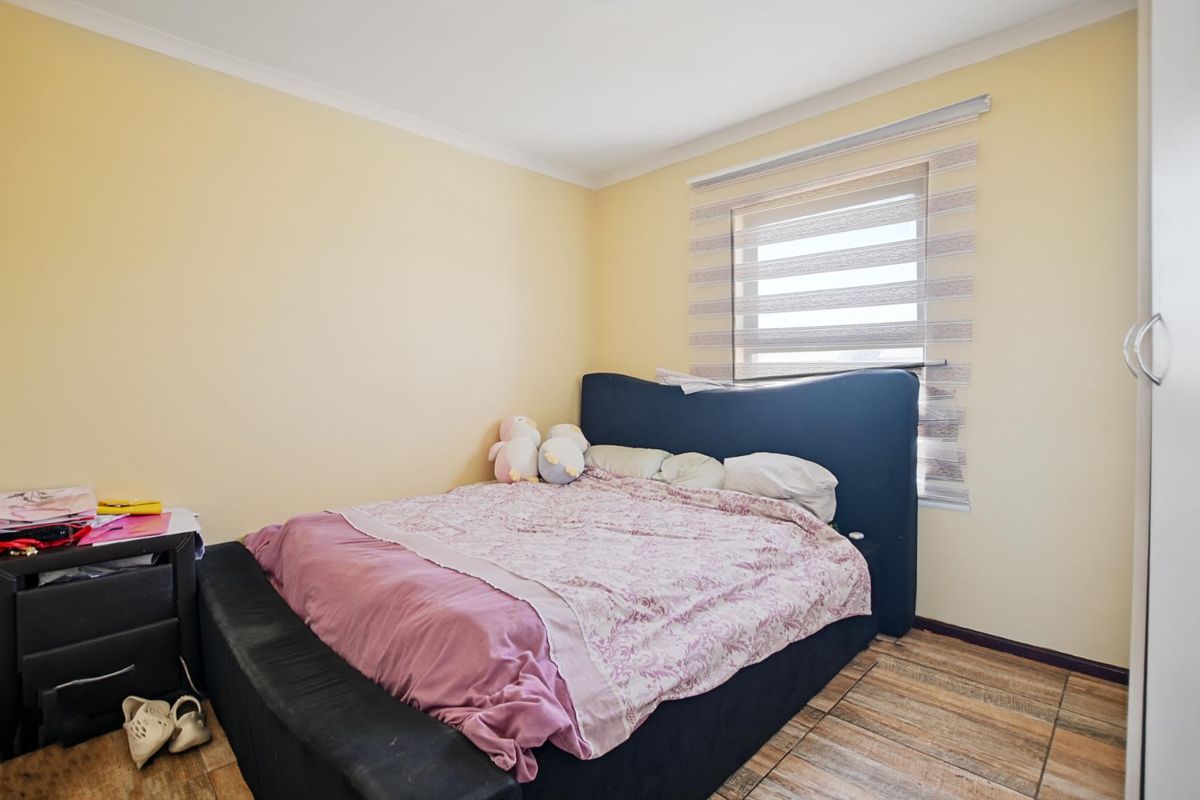 A functional bedroom featuring tiled flooring, neutral wall finishes, and a window fitted with modern roller blinds.