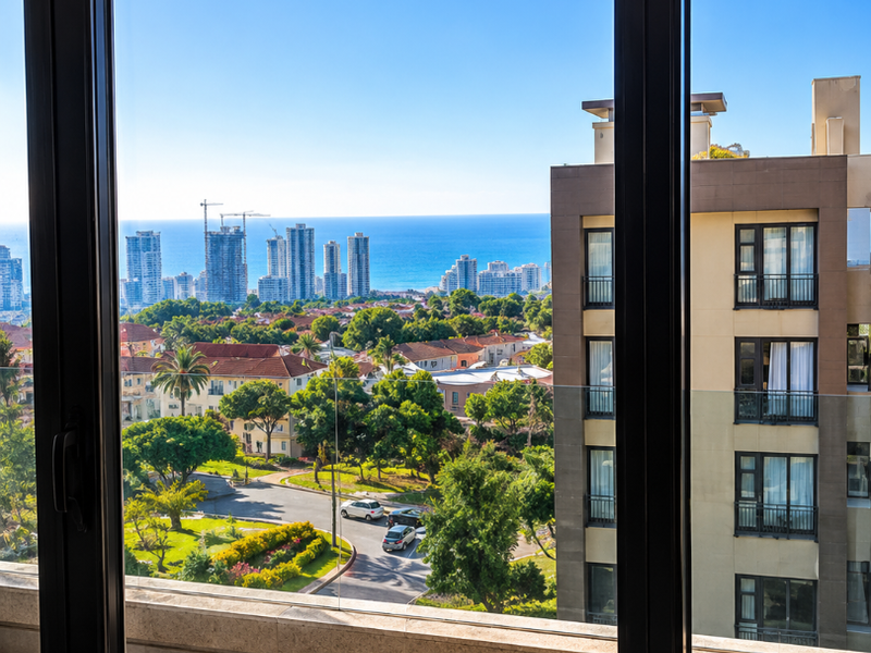A clear view from a balcony overlooking a landscaped residential area, city skyline, and the ocean in the distance.