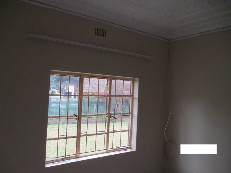 An empty bedroom featuring a steel-framed window with security bars, a curtain rail, and a textured ceiling, requiring minor cosmetic updates.