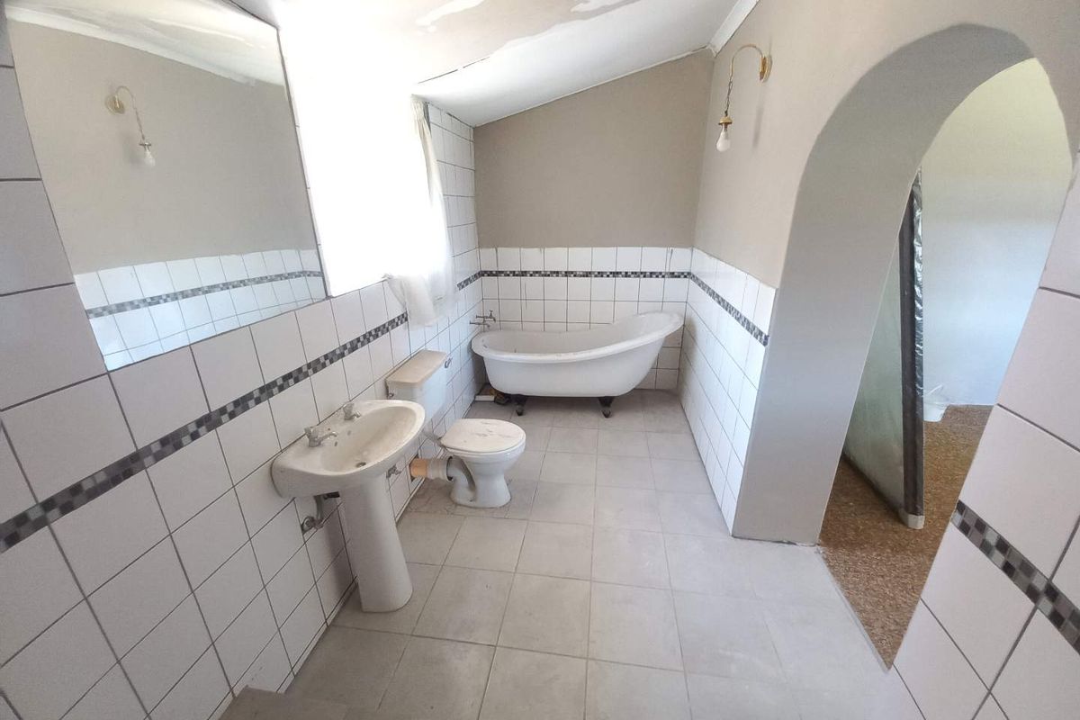 A dated bathroom featuring a clawfoot bathtub, pedestal basin, and toilet, with visible ceiling water damage and tiled walls.