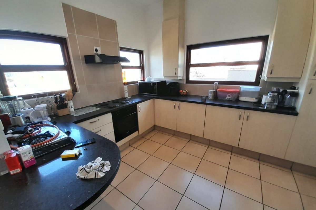 A functional kitchen featuring U-shaped cabinetry, dark countertops, built-in oven, hob, and extractor fan with tiled flooring and ample natural light.